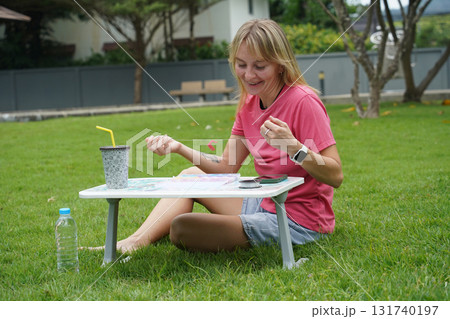 Young woman beading colorful bracelets outdoors in a park Young woman beading colorful bracelets outdoors in a park 131740197