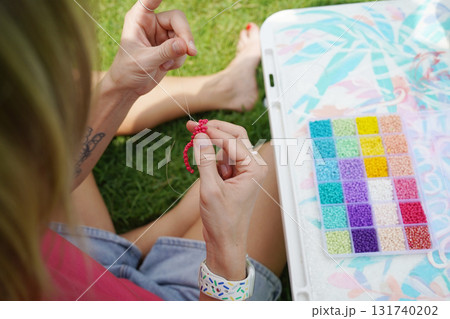 Young woman beading colorful bracelets outdoors in a park 131740202
