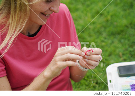 Young woman beading colorful bracelets outdoors in a park Young woman beading colorful bracelets outdoors in a park 131740205