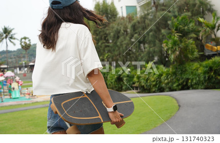A woman is walking at the city park while carrying a skateboard in her hands A woman is walking at the city park while carrying a skateboard in her hands 131740323