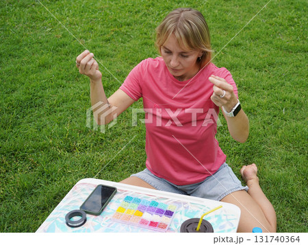 Young woman beading colorful bracelets outdoors in a park Young woman beading colorful bracelets outdoors in a park 131740364