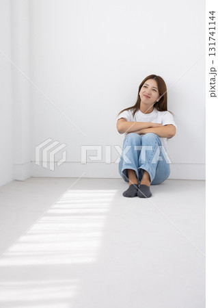 窓から光が差し込む明るい室内で床に座って微笑む若い女性 131741144