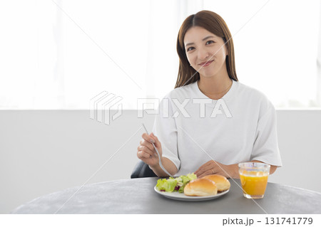 窓から光が差し込む明るい部屋でヘルシーな朝食をとる若い女性 窓から光が差し込む明るい部屋でヘルシーな朝食をとる若い女性 131741779