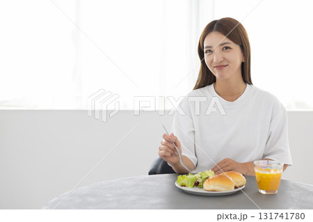 窓から光が差し込む明るい部屋でヘルシーな朝食をとる若い女性 窓から光が差し込む明るい部屋でヘルシーな朝食をとる若い女性 131741780