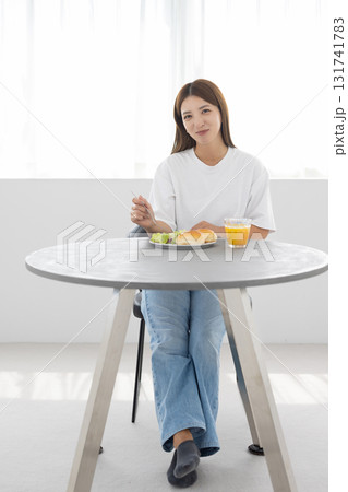 窓から光が差し込む明るい部屋でヘルシーな朝食をとる若い女性 窓から光が差し込む明るい部屋でヘルシーな朝食をとる若い女性 131741783