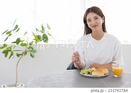 窓から光が差し込む明るい部屋でヘルシーな朝食をとる若い女性 窓から光が差し込む明るい部屋でヘルシーな朝食をとる若い女性 131741784