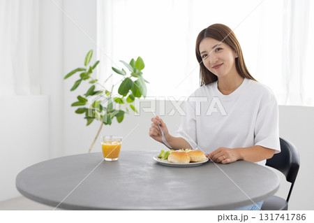 窓から光が差し込む明るい部屋でヘルシーな朝食をとる若い女性 131741786