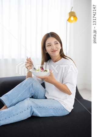 ソファに座って野菜サラダを食べる若い女性 131742147