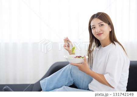 ソファに座って野菜サラダを食べる若い女性 ソファに座って野菜サラダを食べる若い女性 131742149