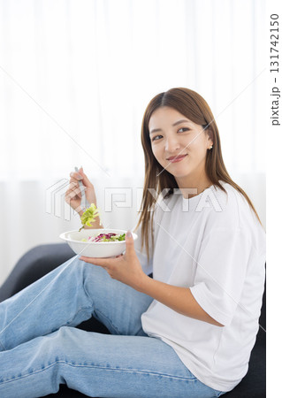 ソファに座って野菜サラダを食べる若い女性 ソファに座って野菜サラダを食べる若い女性 131742150