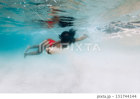 Woman in red swimsuit and mask glides underwater in tropical waters with sandy sea bottom Woman in red swimsuit and mask glides underwater in tropical waters with sandy sea bottom 131744144