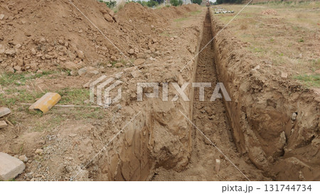 A freshly dug trench cutting through dry earth in a rural construction site 131744734