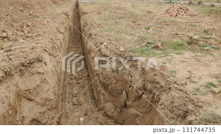 Perspective view of a newly dug trench in a dirt field under daylight conditions 131744735