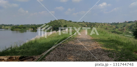 A scenic view of a dirt path alongside a lake with grassy hills in the background A scenic view of a dirt path alongside a lake with grassy hills in the background 131744748