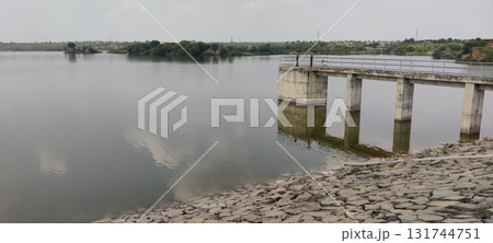 A view of a calm lake with a concrete structure extending into the water and rocks shore 131744751