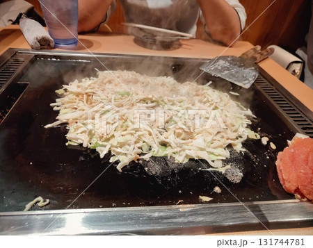 Traditional Japanese okonomiyaki being cooked on a teppan grill, showing delicious texture and authentic street food style. 131744781