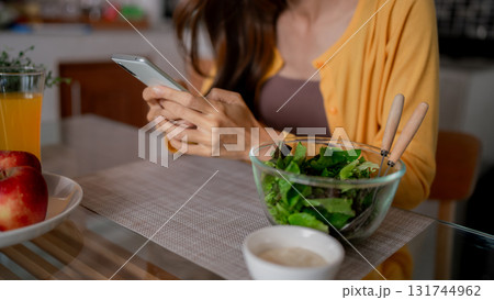 Asian adult woman enjoy healthy meal home casual browse smartphone digital communication technology fresh green salad 131744962