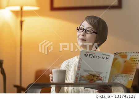 夜にリビングで料理のレシピ本を見るシニア女性 131745128