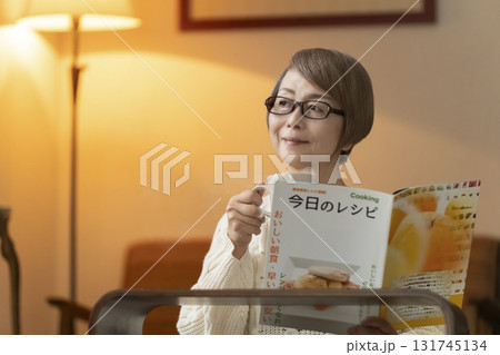 夜にリビングで料理のレシピ本を見るシニア女性 131745134