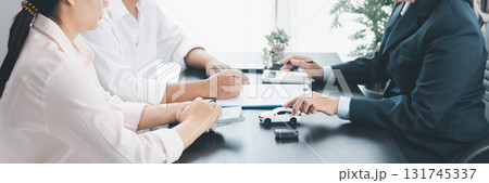Panorama view of business meeting with car loan agreement, dealer showing calculator to customers at office desk with vehicle model and key, concept of auto finance, leasing or insurance. car loan. 131745337