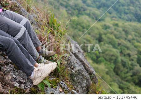 Close up of hiker resting on rocky cliff in hiking shoes, symbol of adventure, outdoor lifestyle, challenge, exploration, determination, nature journey and freedom in mountain travel. Close up of hiker resting on rocky cliff in hiking shoes, symbol of adventure, outdoor lifestyle, challenge, exploration, determination, nature journey and freedom in mountain travel. 131745446