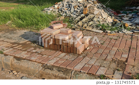 Construction site with stacked red bricks on newly built pathway surrounded by rubble and dry grass in daylight 131745571