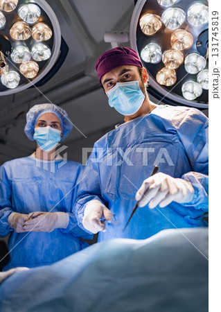 A surgeon and assistant are in an operating room, performing a procedure under bright lights. A surgeon and assistant are in an operating room, performing a procedure under bright lights. 131745819