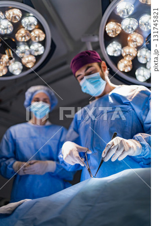 A surgeon is performing surgery in an operating room, with a surgical assistant present. A surgeon is performing surgery in an operating room, with a surgical assistant present. 131745821