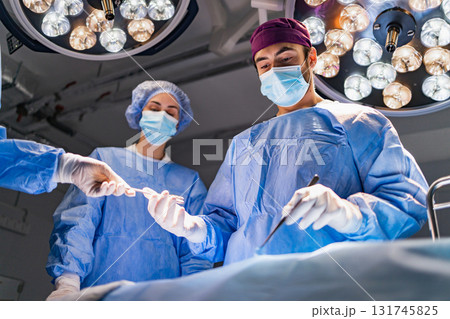 A surgical team is focused during an operation in a modern operating room, with bright lights overhead. A surgical team is focused during an operation in a modern operating room, with bright lights overhead. 131745825