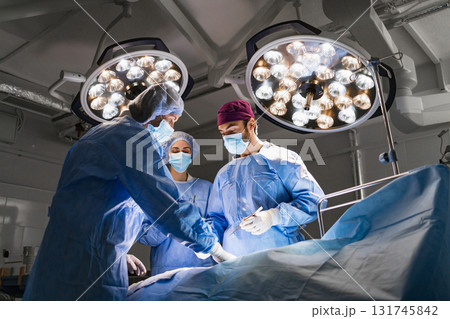 Medical team performing surgery in a modern operating room, illuminated by surgical lights. 131745842