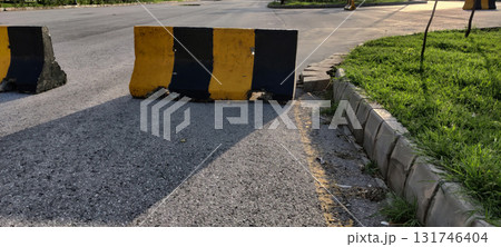Road safety barrier painted in black and yellow stripes on asphalt with curb and grass in gentle afternoon lighting Road safety barrier painted in black and yellow stripes on asphalt with curb and grass in gentle afternoon lighting 131746404