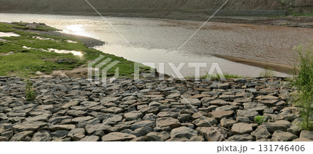Peaceful river curve with scattered green grass and gray stones under golden sky during tranquil early morning or sunset 131746406