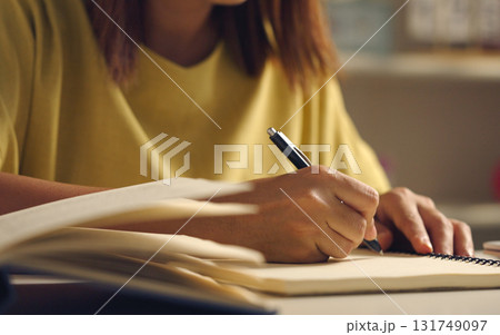Asian woman works from home, surrounded by notes, a laptop, and messages. She browses the internet, writes ideas, and researches for her startup, utilizing wireless technology. 131749097