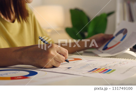 Asian woman works from home, surrounded by notes, a laptop, and messages. She browses the internet, writes ideas, and researches for her startup, utilizing wireless technology. Asian woman works from home, surrounded by notes, a laptop, and messages. She browses the internet, writes ideas, and researches for her startup, utilizing wireless technology. 131749100