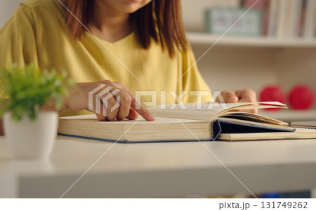 Close up of Asian woman reading a book on desk at home. Lifestyle and education concept. Close up of Asian woman reading a book on desk at home. Lifestyle and education concept. 131749262