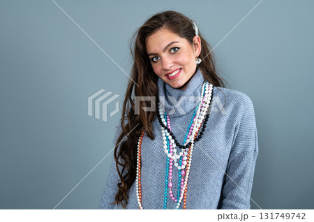 elegant woman in a long gray sweater has fun with many bead chains and jewelry, isolated on gray 131749742