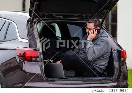 a man sitting in the open trunk of a car and working with a laptop, mobile technology, remote work a man sitting in the open trunk of a car and working with a laptop, mobile technology, remote work 131749984