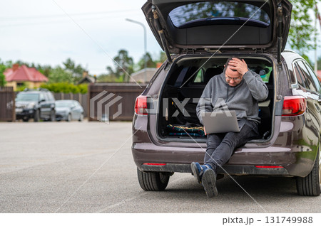 a man sitting in the open trunk of a car and working with a laptop, mobile technology, remote work a man sitting in the open trunk of a car and working with a laptop, mobile technology, remote work 131749988