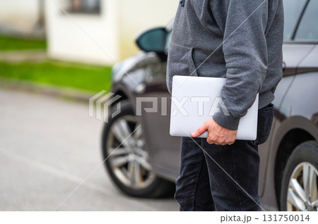 a man silhouette with a computer in his hands on the street and a car in the background 131750014