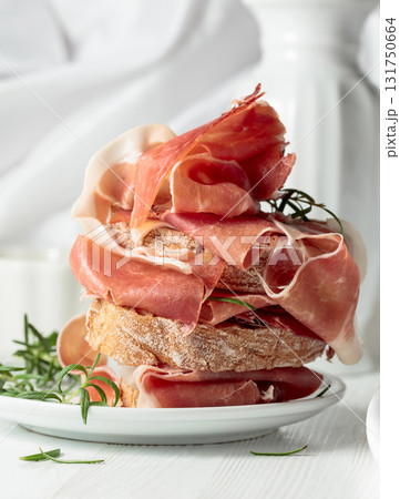 Ciabatta with prosciutto and rosemary on a white wooden table. Ciabatta with prosciutto and rosemary on a white wooden table. 131750664