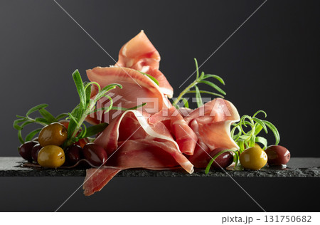 Prosciutto with olives and rosemary on a black background. 131750682