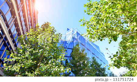 Glass office building surrounded with green trees. Eco-friendly office building. Sustainable architecture of city reducing heat carbon dioxide modern city environment. Glass office building surrounded with green trees. Eco-friendly office building. Sustainable architecture of city reducing heat carbon dioxide modern city environment. 131751724