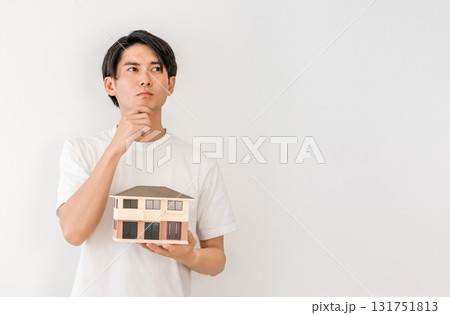 住宅模型を持って悩む若いアジア人男性(マイホーム,一戸建て) 住宅模型を持って悩む若いアジア人男性(マイホーム,一戸建て) 131751813