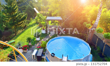 Garden of a suburban house in summer in which you can see a removable swimming pool, pergola in a place with a lot of vegetation. 131752704