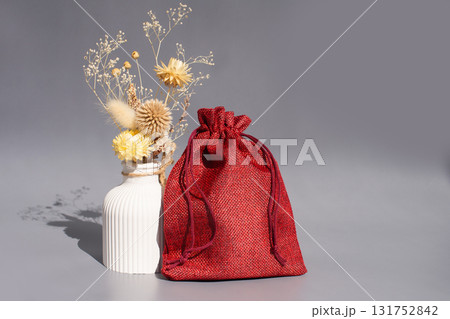 Red drawstring bag with dried flowers in ceramic vase on gray background Red drawstring bag with dried flowers in ceramic vase on gray background 131752842