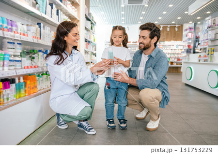 Smiling woman in lab coat advising man and child indoors in modern drugstore 131753229