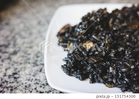 Spanish black rice with squid ink served on a white plate, traditional Mediterranean seafood dish 131754300
