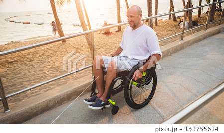 Disabled man in a wheelchair moves on a ramp to the beach. Disabled man in a wheelchair moves on a ramp to the beach. 131755614