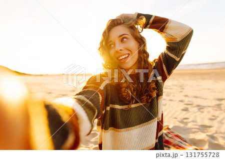 Young woman taking a cheerful selfie on a sandy beach during sunset. Lifestyle, travel, active life 131755728