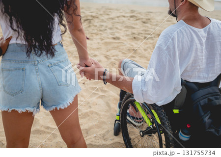 Disabled man in a wheelchair with his wife on the beach. Disabled man in a wheelchair with his wife on the beach. 131755734